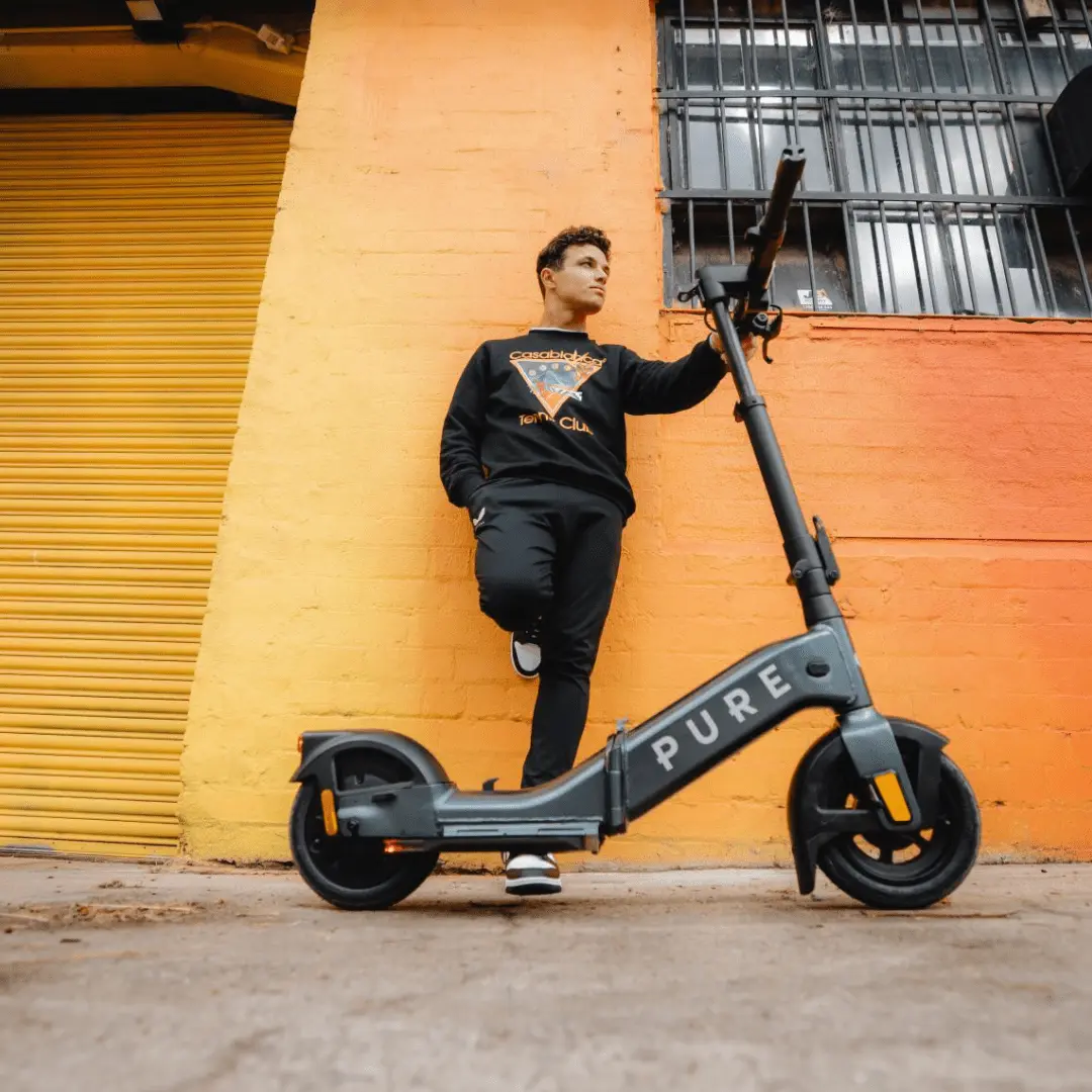 PURE Advance Flex E-Scooter in Mercury Grey mit Lando Norris an der Wand stehend